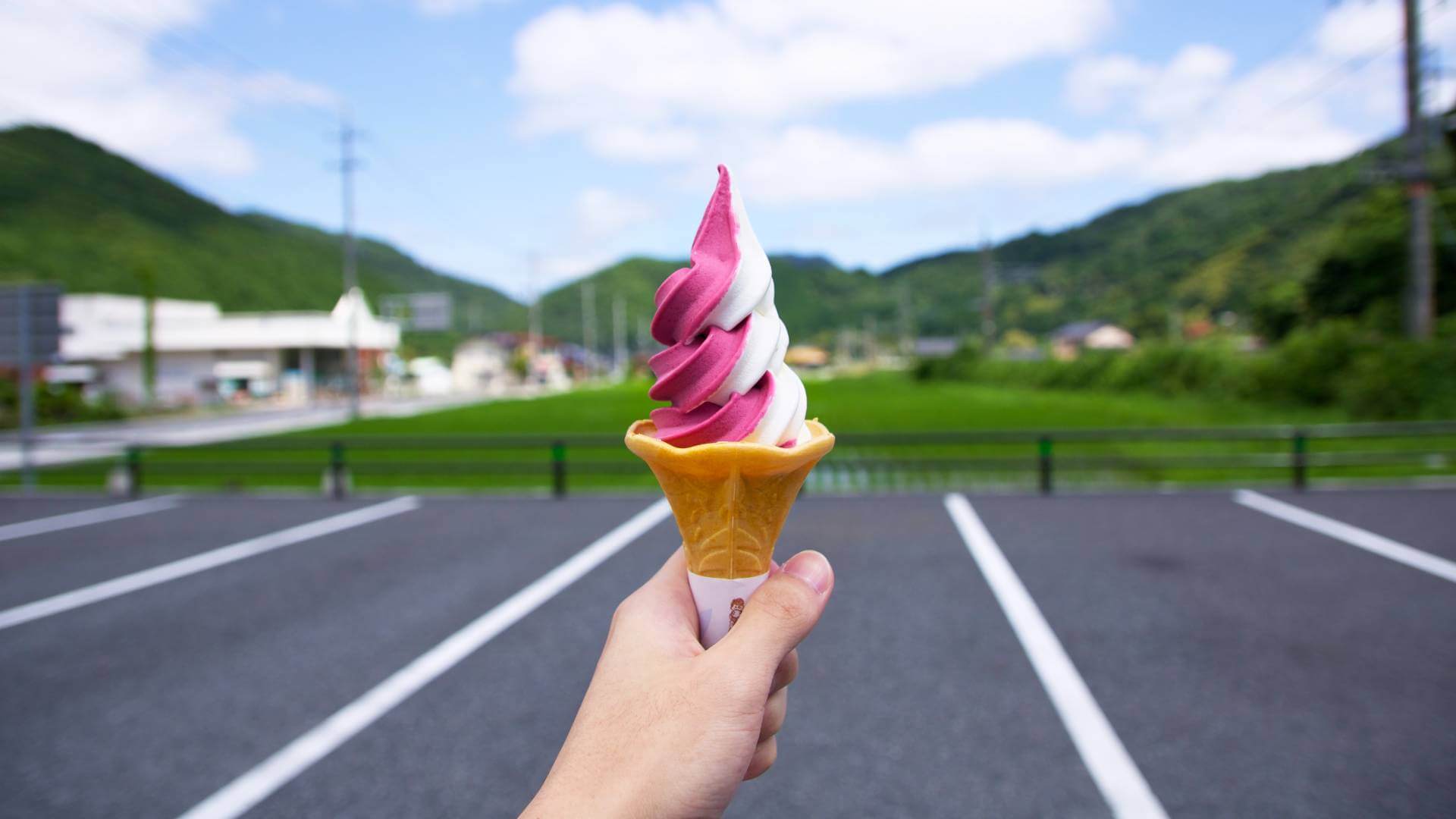 Main qui tient un cornet de crème glacée torsadé blanc et rose à l'extérieur